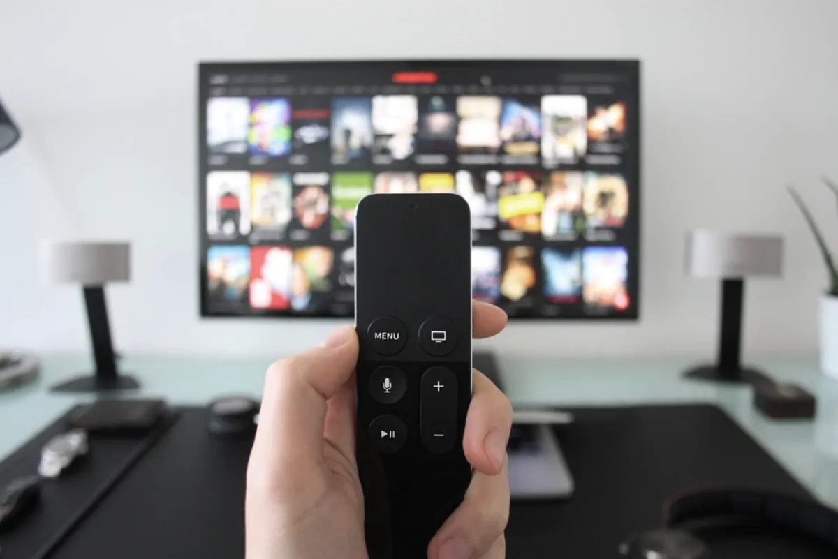Hand holding a voice remote in front of a smart TV, illustrating Samsung TV microphone spying claims