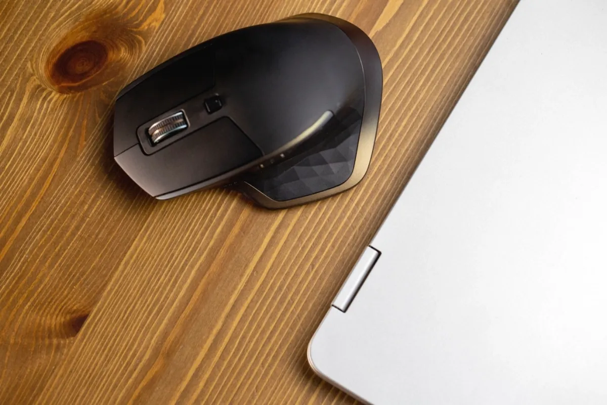 Silver laptop and mouse on a wooden desk, illustrating the touchscreen MacBook Pro launch